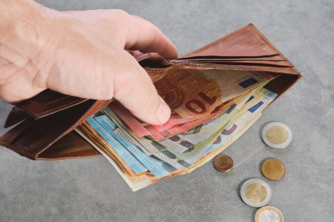 Senior man holds a wallet with euro banknotes in his hand, euro banknotes in the wallet. Wallet with money in a man’s hand, background idea of paying taxes, buying or paying for services